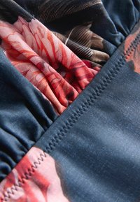 Tessuto misto cotone con base blu scuro e motivi floreali nelle tonalità del rosa e del rosso, con texture arricciata e dettagli di cuciture a contrasto.