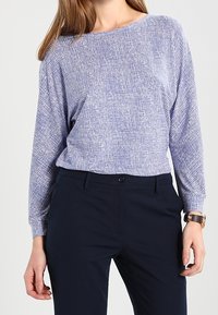 Camisa ligera de manga larga con un patrón texturizado en azul y blanco; corte suelto; combinada con pantalones oscuros azul marino; diseño minimalista.