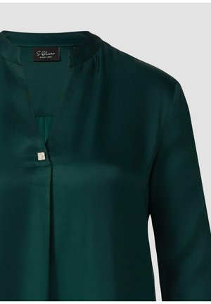 Blouse vert foncé en tissu lisse, présentant un décolleté en V avec une petite décoration carrée à la nuque. Manches longues.