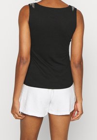 Svart linne med en klassisk rund halsringning, med strukturerade utsmyckningar på axlarna. Kombinerat med vita, lätta shorts.