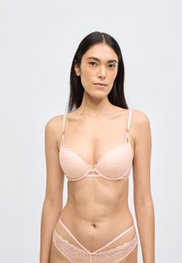Világos rózsaszín csipke melltartó fogazott szegéllyel, alátámasztó merevítőkkel és állítható pántokkal, hozzáillő geometriai mintájú csipke bugyival.
