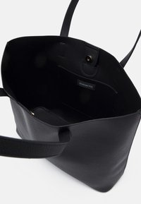 Černá kožená taška přes rameno s texturovaným povrchem, otevřeným designem a vnitřní kapsou se štítkem. Dvě dlouhé popruhy pro nošení.