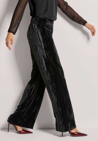 Zwarte fluwelen wijde broek met verticale strepen, voorzien van een geplooide tailleband. Gecombineerd met glanzende rode stiletto hakken.