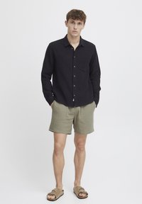 Chemise noire à boutons avec un tissu texturé, manches courtes et une poche poitrine, associée à un short vert clair avec une coupe ample et deux poches.