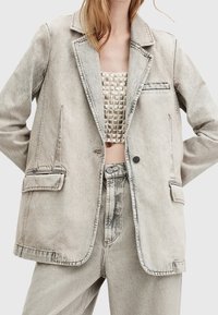 Vaaleanharmaa farkkutakki, jossa on jämäkkä muotoilu, lovetetut kaulukset, kaksi etutaskua ja kontrastiväriset tikkaus. Kevyt ja ylisuuri malli.