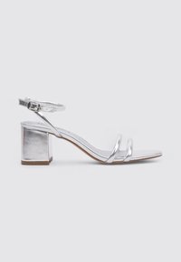 Sandal con tiras plateadas y tacón cuadrado, que cuenta con una correa en el tobillo con hebilla y un diseño elegante y minimalista. Acabado metálico suave.