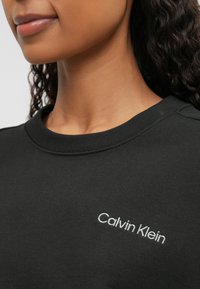 Μαύρη μπλούζα με στρογγυλή λαιμόκοψη, με λευκό κεντητό λογότυπο "Calvin Klein" στο στήθος. Απαλή, λεία υφή υφάσματος.