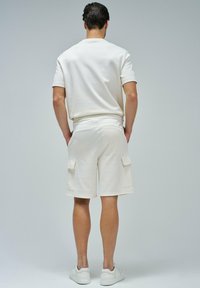 T-shirt en mélange de coton couleur crème et shorts cargo assortis avec deux poches latérales. La tenue présente une coupe décontractée et une taille élastique.