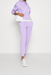 Lila huvtröja med snörning, i kombination med lila joggingbyxor. Vita sneakers och en liten vit crossbody-väska fulländar looken. Mjuk bomullsmaterial.