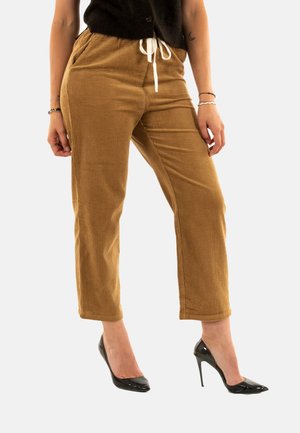 Bruine corduroy broek met een rechte pijp, voorzien van een witte trekkoord en voorzakken, gecombineerd met zwarte hoge hakken.