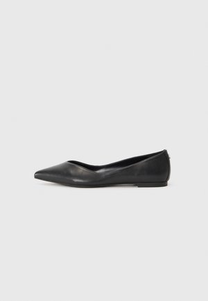 Chaussure plate en cuir noir à bout pointu avec un petit talon et une couture minimaliste sur un fond gris clair uni.