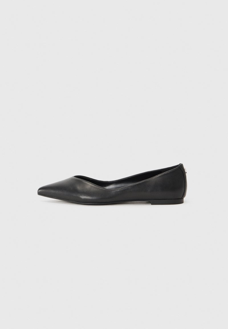Chaussure plate en cuir noir à bout pointu avec un petit talon et une couture minimaliste sur un fond gris clair uni.