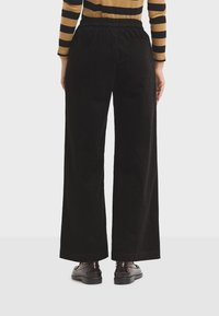 Black corduroy wide-leg pants with an elastic waistband and side pocket, paired with a striped long-sleeve top and dark shoes.