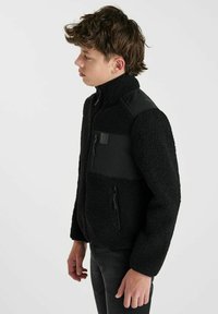 Zwarte fleecejas van textiel met een hoge kraag en een zwart synthetisch paneel op de borst, voorzien van een ritssluiting zak en logodetail.