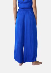 Pantalons à jambes larges bleus en tissu léger avec une taille élastique, présentant une texture lisse et un design fluide.