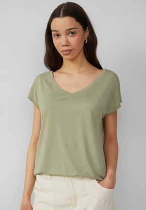 T-shirt vert clair à manches courtes et col en V, fabriqué en tissu doux et texturé, associé à un pantalon de couleur claire avec une coupe décontractée.