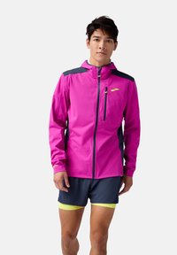 Bright pink running jacket with dark gray accents, full zip, hood, and reflective details. Paired with navy shorts and yellow trim.