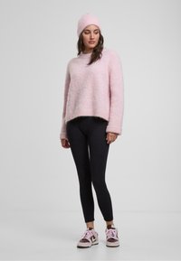 Kerge roosa, karvane kudum, millel on ümmargune kaelus, kombineeritud mustade leggings'itega ja pruuni/roosa värvi tossudega, koos sobiva nokamütsiga.