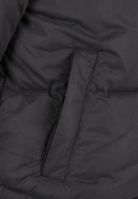 Sort dunjakke stof har en glat tekstur med en sidelomme markeret af en kontrastfarvet søm, hvilket fremhæver dets funktionelle design.