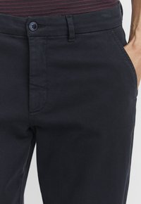 Pantalons bleu marine en tissu lisse, dotés d'une fermeture à bouton unique et de poches latérales ; design à jambe droite avec une coupe classique.