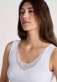 Witte tanktop met een bloemenkant halslijn. De stof lijkt glad en zacht, met een klassiek mouwloos ontwerp en een ronde halslijn.