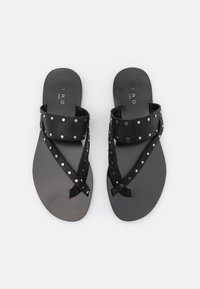 Sandales en cuir noir avec des brides studded et tressées, semelle plate et design minimaliste. Accents texturés sur la bride supérieure.