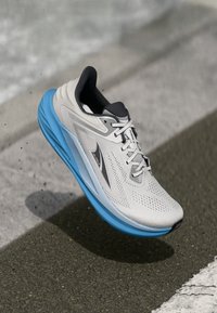 Chaussure de course gris clair avec une semelle bleue, dotée d'un dessus en maille respirante, d'un système de laçage et d'un design aérodynamique élégant.
