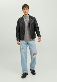 Chaqueta de moto de cuero negra, camiseta gris, jeans claros desgastados y zapatos negros; con cremalleras y desgarros visibles en el denim.