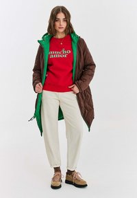 Hnedý pufový kabát so zelenou podšívkou, červená mikina s bielym textom, krémové nohavice a hnedé topánky s ružovými šnúrkami. Jednoduchý dizajn a textúry.