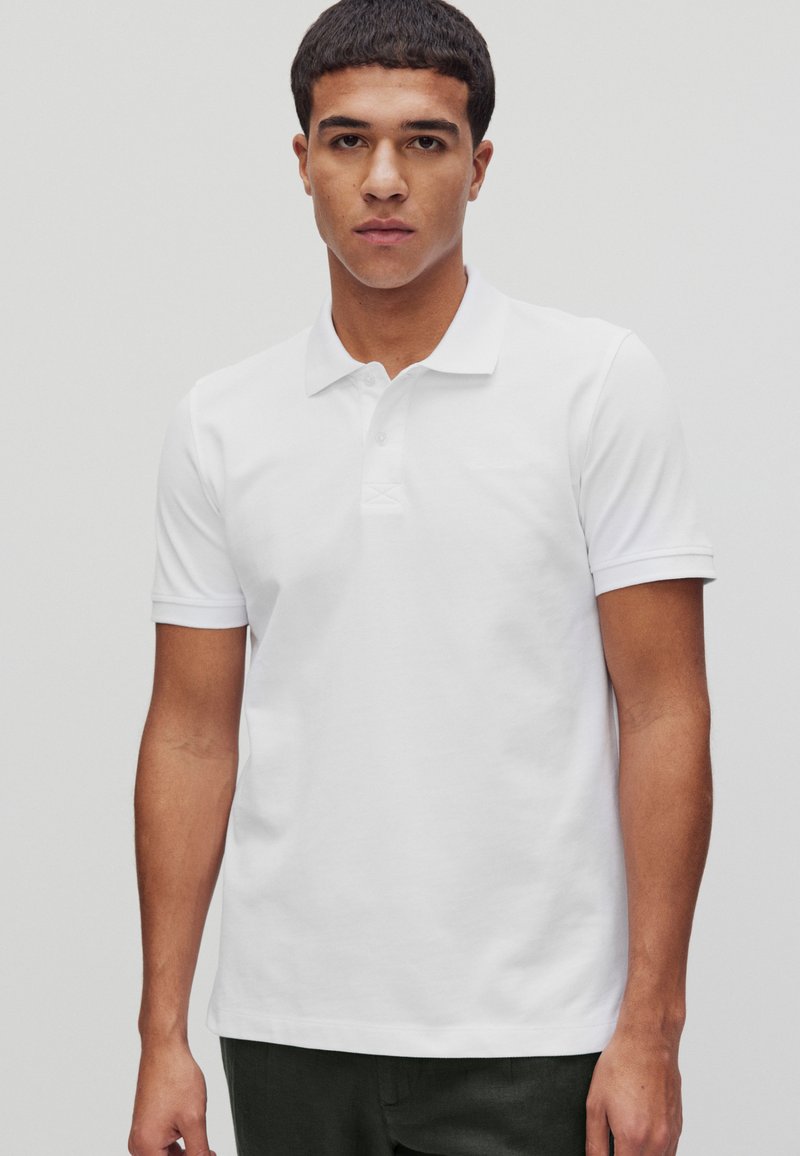 Vit pikétröja med klassisk krage, korta ärmar och knappslå. Mjuk bomullstyg med en lätt textur.