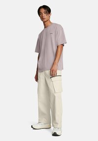 Ljuslila oversized t-shirt med en liten logotyp, ihopparad med krämfärgade cargobyxor med sidofickor och kontrasterande dragkedjor, bärs med vita sneakers.
