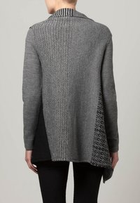 Grå, asymmetrisk cardigan med patchworkdesign, varierande texturer och mönster, långa ärmar och sjalkrage.