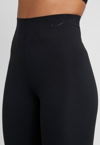 Czarne legginsy o wysokim stanie z elastycznego materiału. Posiadają małe, wytłoczone logo Nike na pasku. Gładka tekstura bez wzorów.
