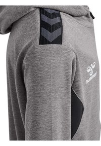 Grå atletisk hoodie med tekstureret stof, der har en sort chevronmønster accent på skulderen og en sort sidepanel for kontrast.