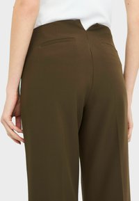 Pantaloni marroni a vita alta caratterizzati da una texture liscia, tasche laterali discrete e una vestibilità su misura con un design della cucitura posteriore sagomato.