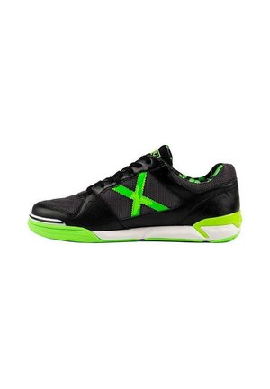 Zapatilla deportiva negra con suela verde, "X" verde en el lateral, cordones negros y forro interior de camuflaje verde, vista desde el lado exterior.
