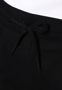 I pantaloni sportivi in cotone neri presentano una vita con cordino e punte nere, una texture liscia e un minimo dettaglio di cucitura.