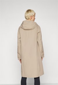 Beige trench coat with a hood, featuring long sleeves and a straight cut. The fabric appears smooth and waterproof.