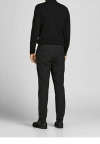 Men's black trousers with a slim fit, featuring a textured pattern, two back pockets, and paired with black shoes, against a light background.