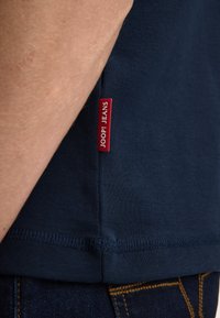 Granatowy bawełniany t-shirt z czerwonym, markowym logo na bocznym szwie; miękka w dotyku tkanina, dopasowany krój i krótkie rękawy.