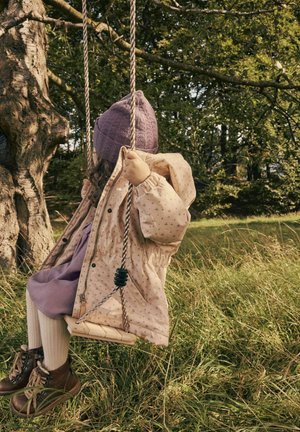 Beige padded jacket with small floral patterns, paired with a purple dress, knitted purple hat, and brown lace-up boots. Swinging in grass.