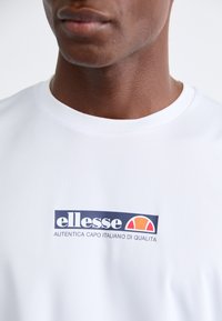 Fehér pamut póló kék és narancssárga "ellesse" logóval. A dizájn kerek nyakkivágással és sima tapintással rendelkezik.