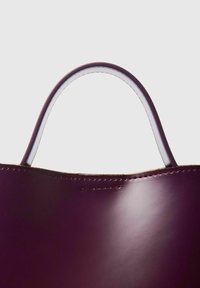 Läderaxelväska i djup burgundy med slät yta, vit sömnad och rundade handtag synliga upptill.