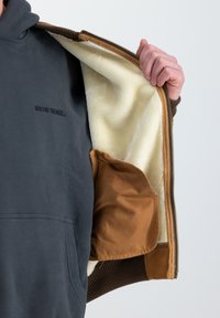 Sudadera con capucha de exterior gris oscuro y forro de piel sintética color crema; presenta un bolsillo de acento marrón y puños de canalé. Cierre de cremallera.