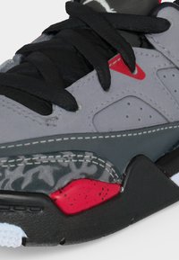 Κοντινό πλάνο στο μπροστινό μέρος του αθλητικού παπουτσιού με μαύρα κορδόνια, γκρι επάνω μέρος, μαύρη σόλα, κόκκινες λεπτομέρειες και τμήμα ενδιάμεσης σόλας με σχέδιο.