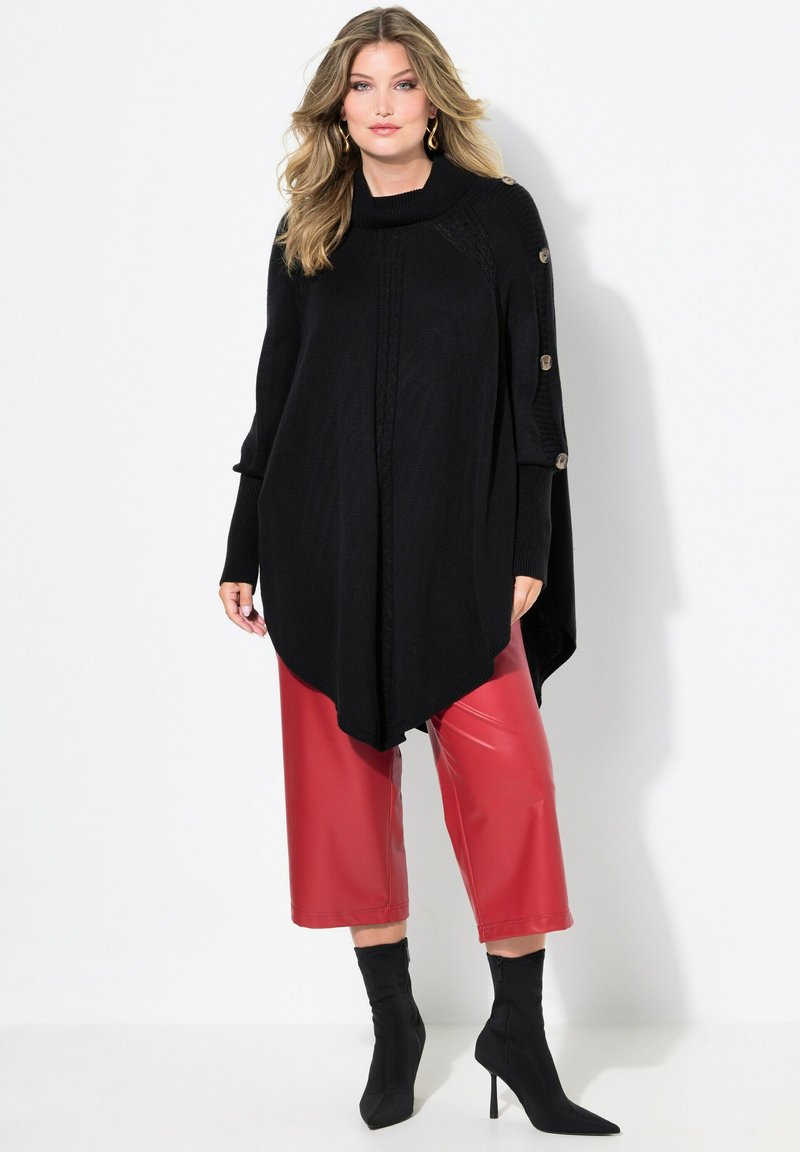 Poncho en tricot noir avec un col cowl, doté de détails en boutons sur l'épaule. Assorti à des culottes rouges brillantes et des bottines noires à bout pointu.