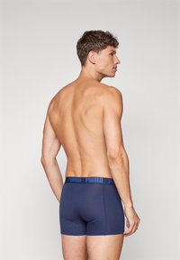 Marina blå boxershorts med en blå märkesmidja. Tyget ser slätt och åtsittande ut, vilket visar en stödjande design. Bakåtsikt presenteras.