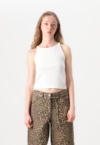 Biely rebrovaný crop top s vysokým výstrihom spárovaný s nohavicami širokého strihu s leopardím vzorom, ktoré majú zapínanie na gombík a voľný strih.