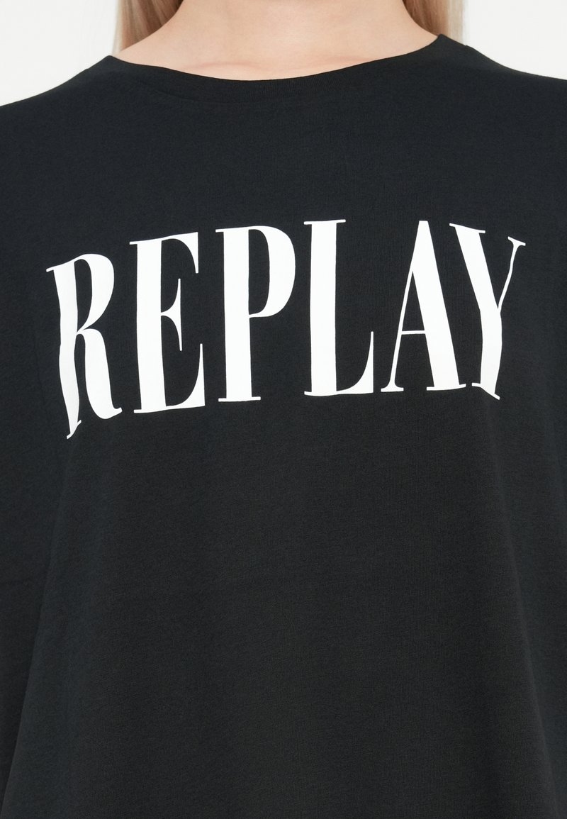 Camiseta de algodón negra con bold texto blanco "REPLAY". Mangas cortas, cuello redondo, textura suave y corte relajado.