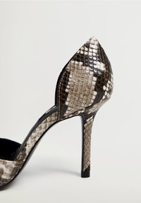 Chaussure à talon avec un bout pointu, présentant un motif en peau de serpent noir et blanc et une finition lisse et brillante. Talon noir haut et élancé.